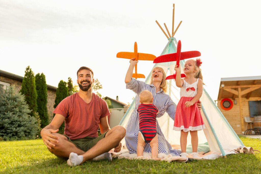 Parents playing with children, throwing toy airplanes while camping in the backyard
